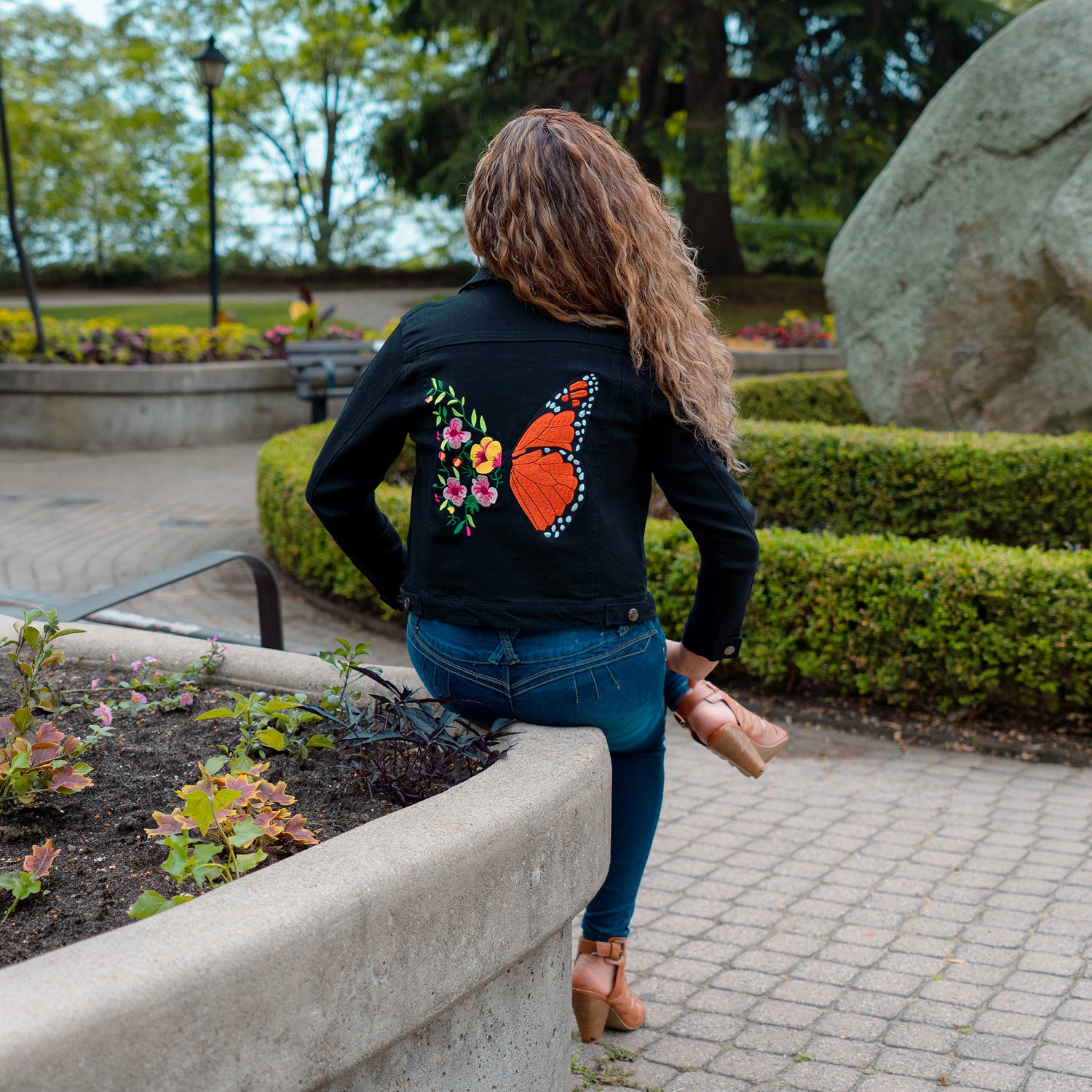 Woman wearing black embroidered jacket with monarch butterfly and floral design in outdoor setting