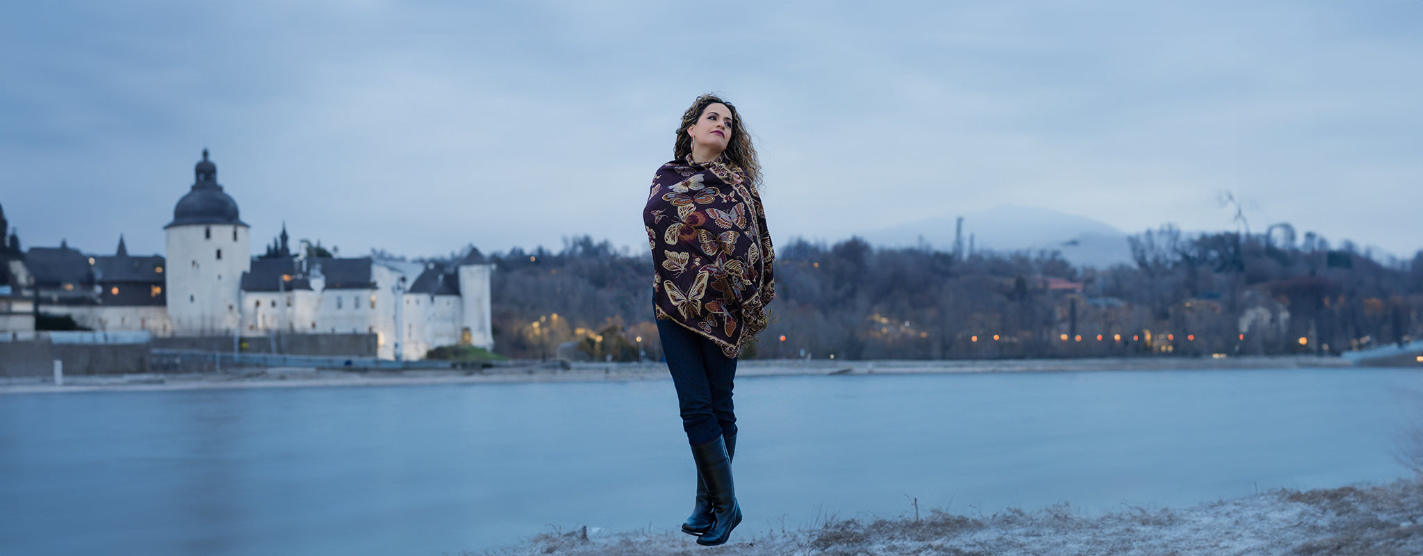 Woman wearing monarch butterfly embroidered shawl by a lake in winter